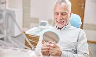 Patient smiling in reflection of handheld mirror